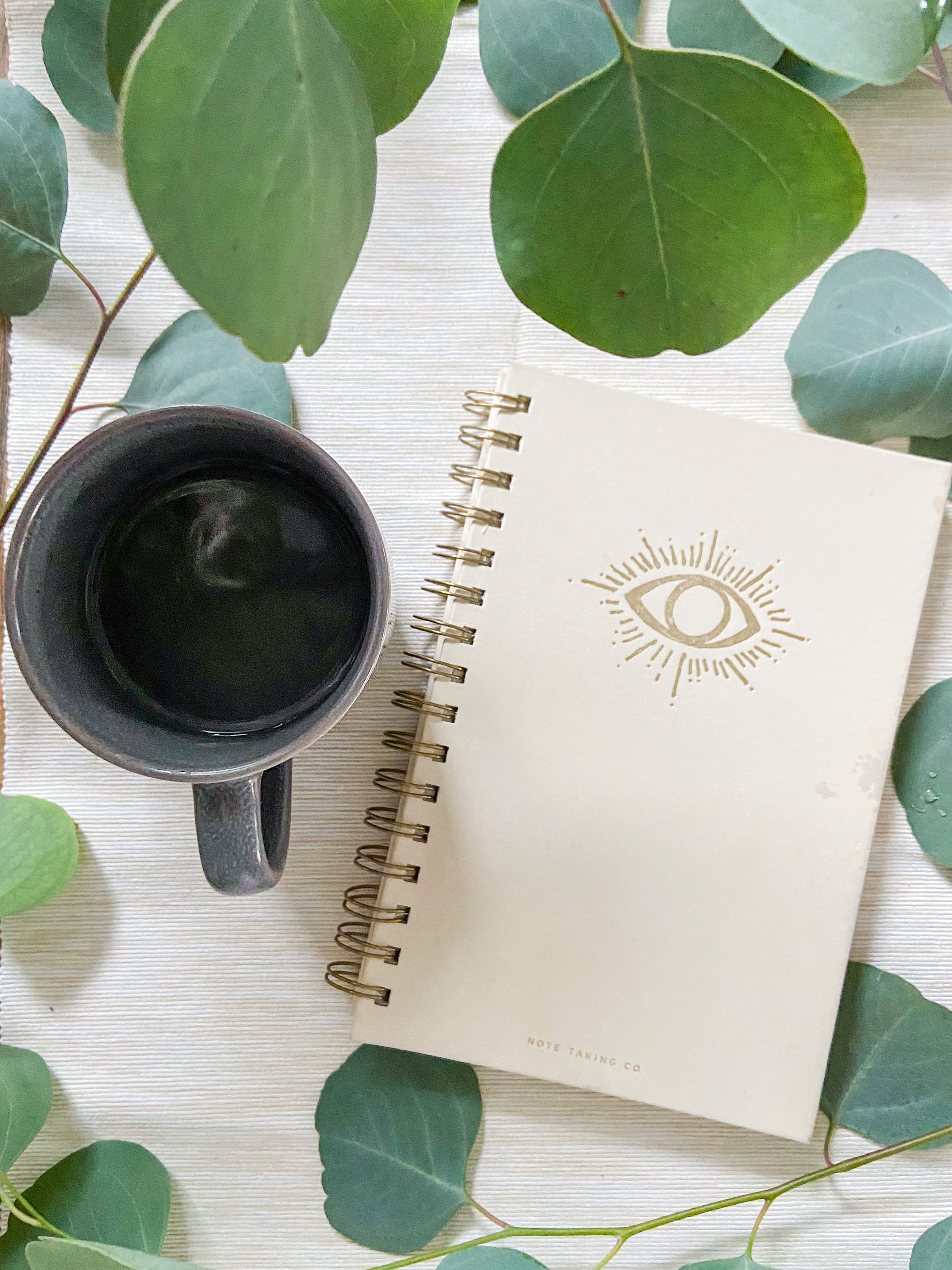 A journal and a cup of coffee resting among eucalyptus leaves